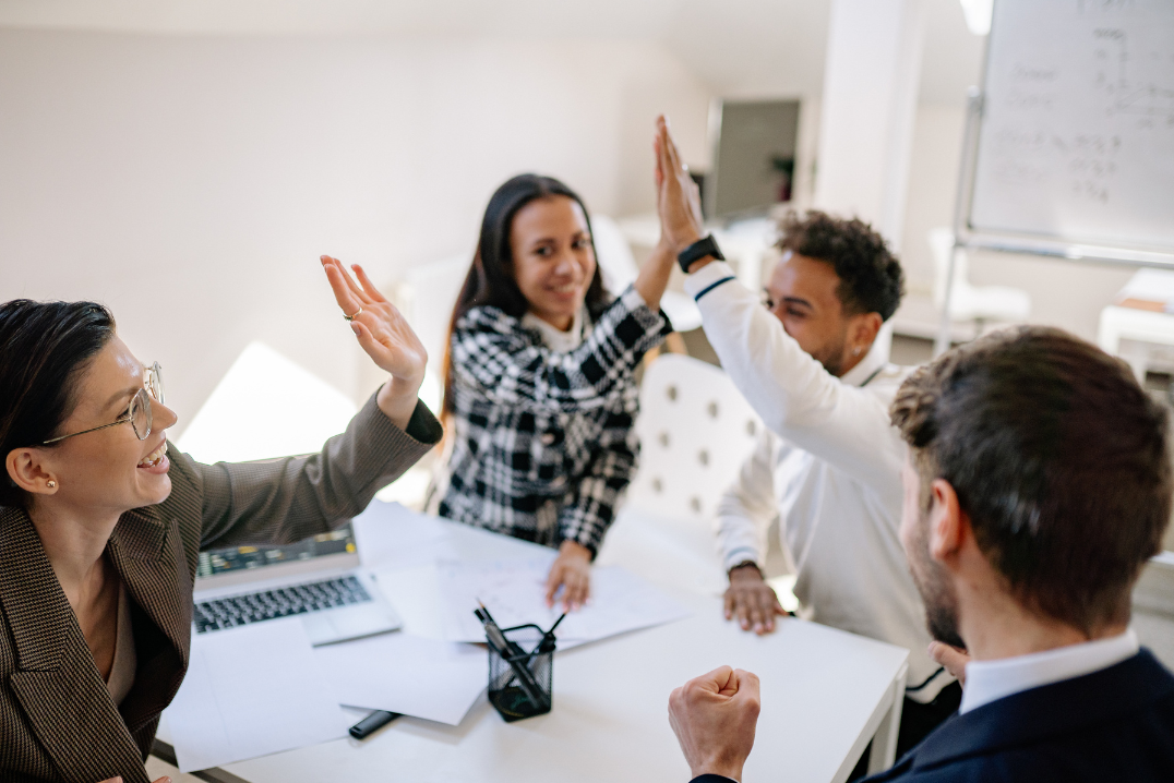 Group of people in a meeting room giving high fives.