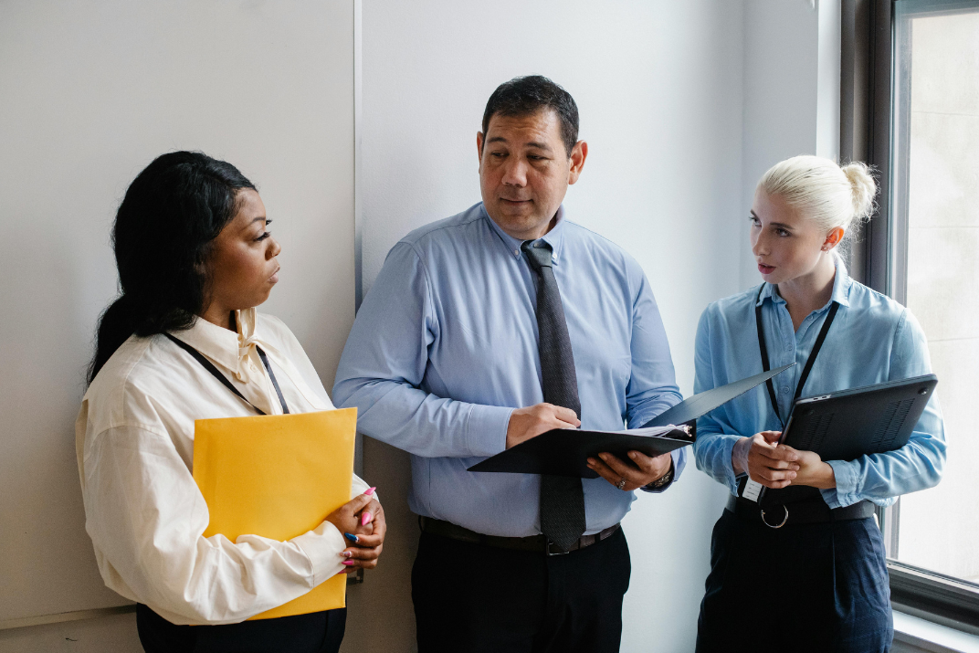 Three professionals in a discussion with documents and folders.